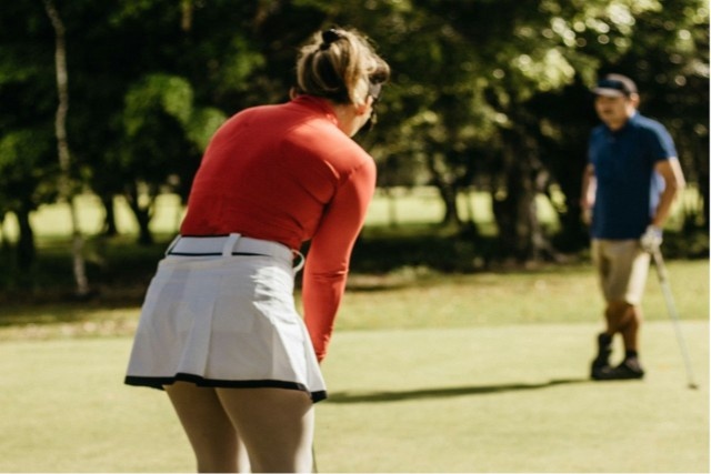 a woman in a red shirt and white skirt playing a game of golf